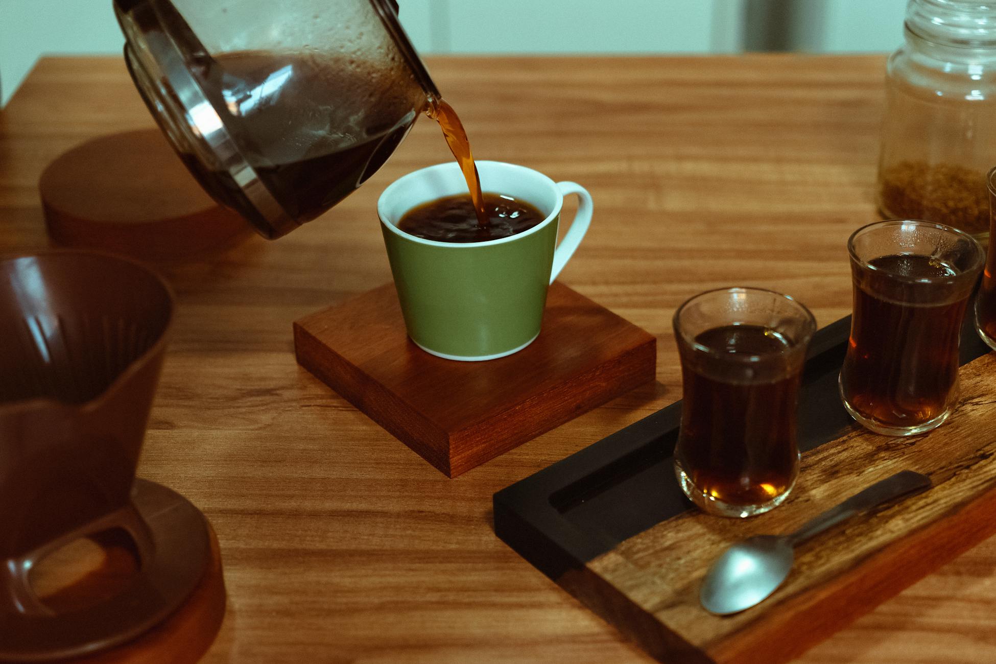 High angle view of coffee being poured into a cup with additional glasses on a wooden tray.