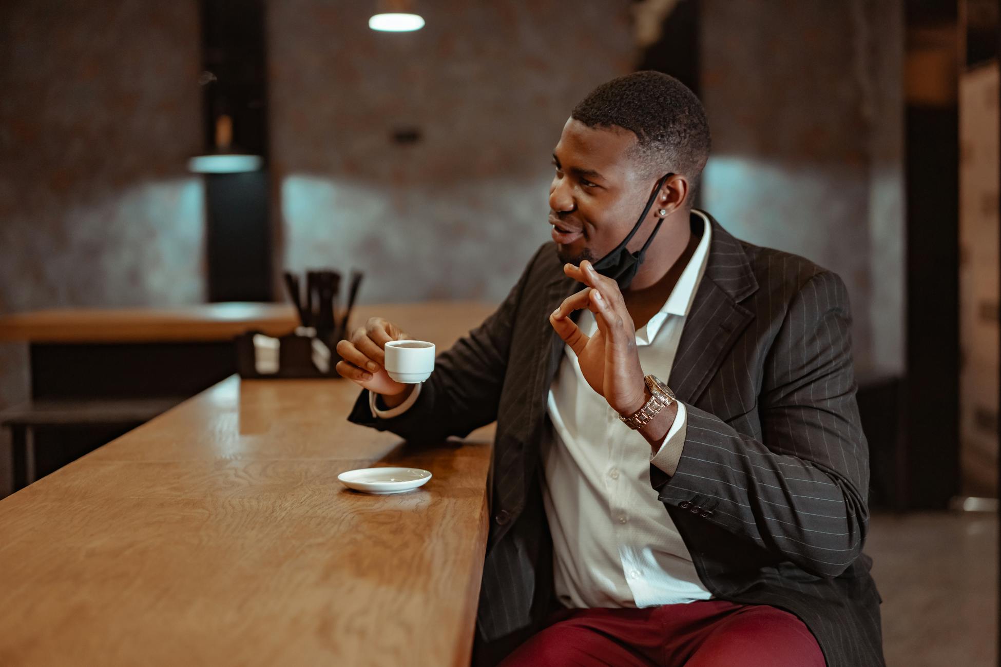 A well-dressed man in a suit enjoying a cup of coffee in a chic indoor cafe setting.