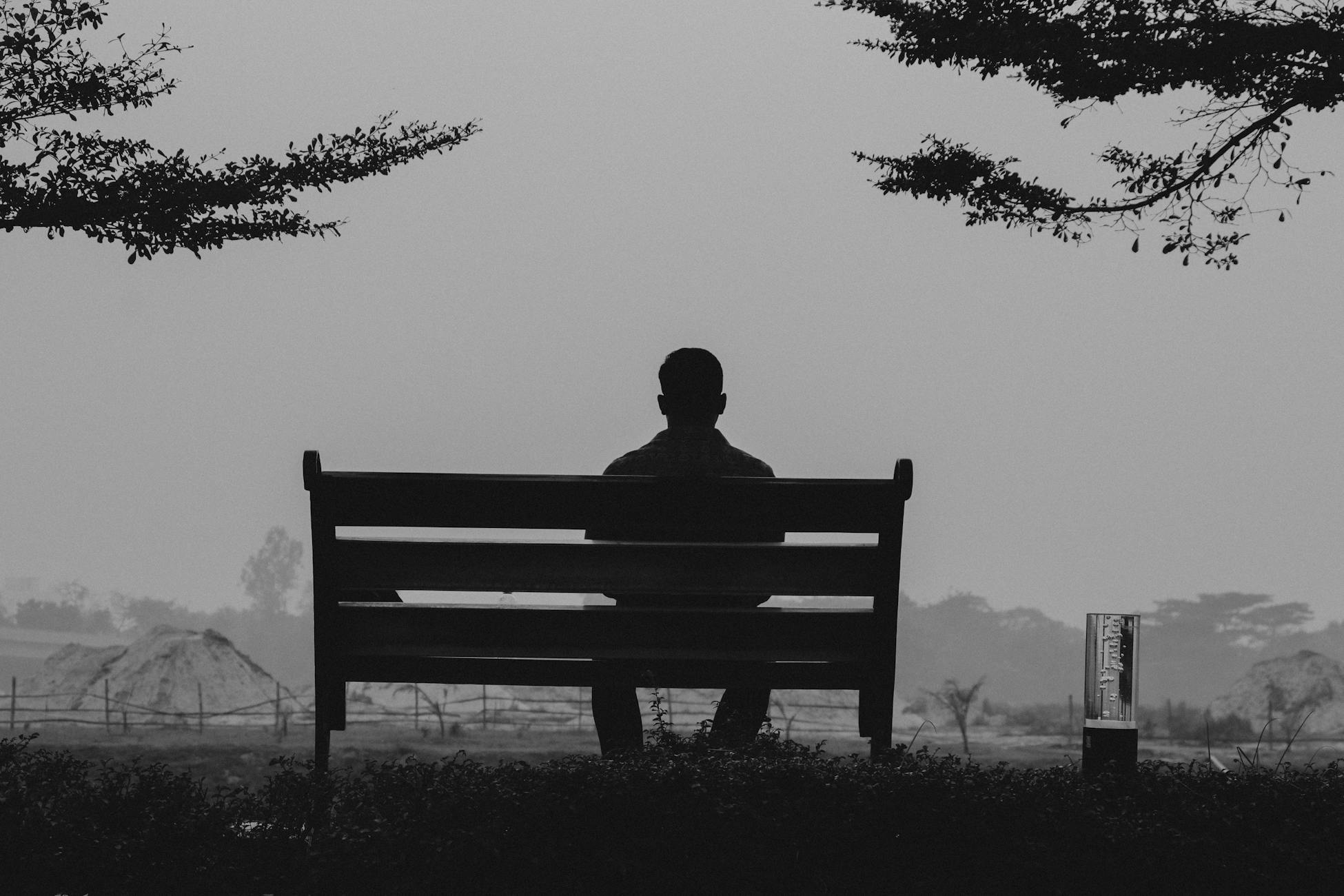 A black and white silhouette of a man sitting on a bench outdoors in Dhaka, Bangladesh.