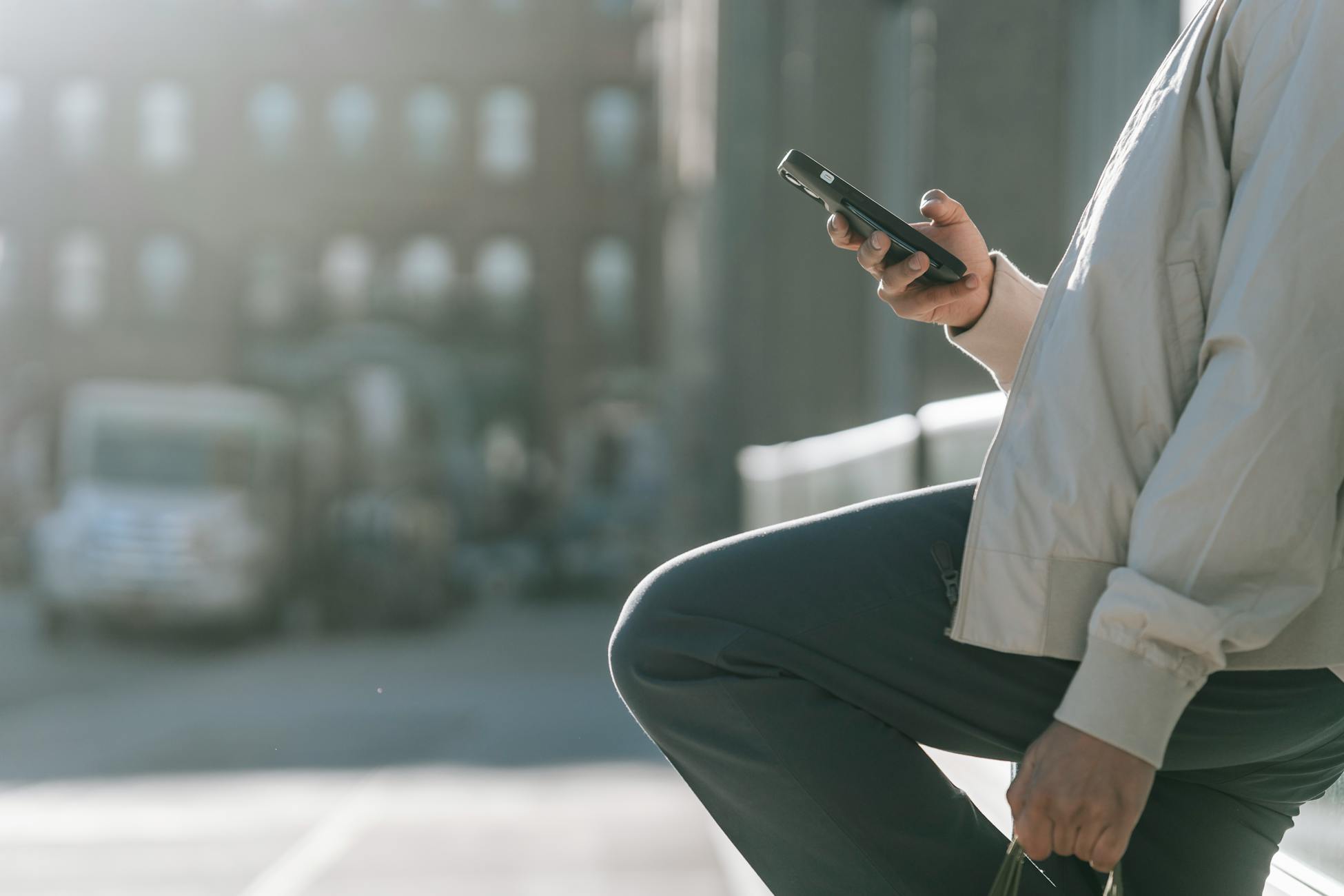 Side view of crop unrecognizable male with raised leg surfing internet on cellphone on roadway in sunny city