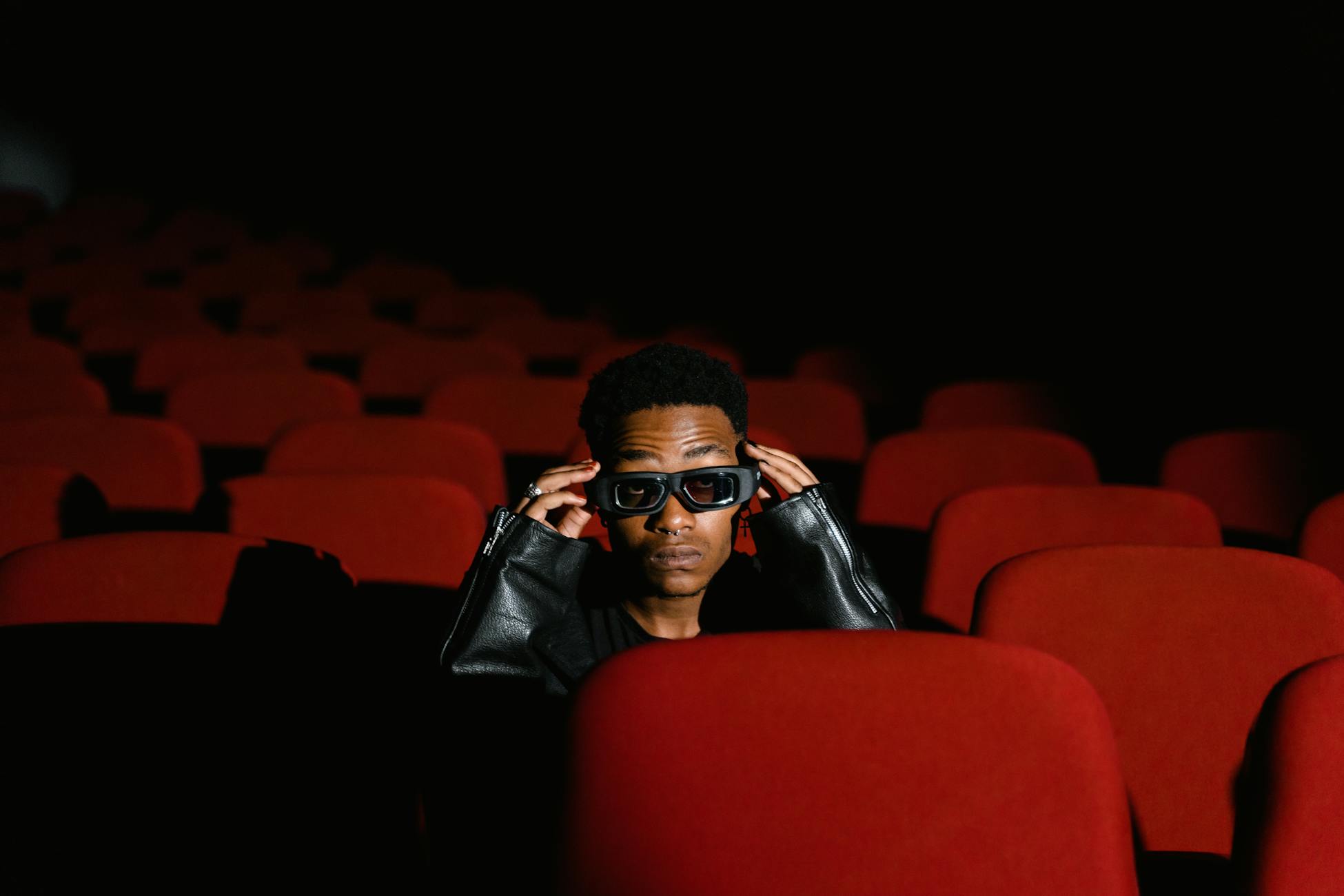 Individual sitting alone in a theater, wearing 3D glasses among red seats.