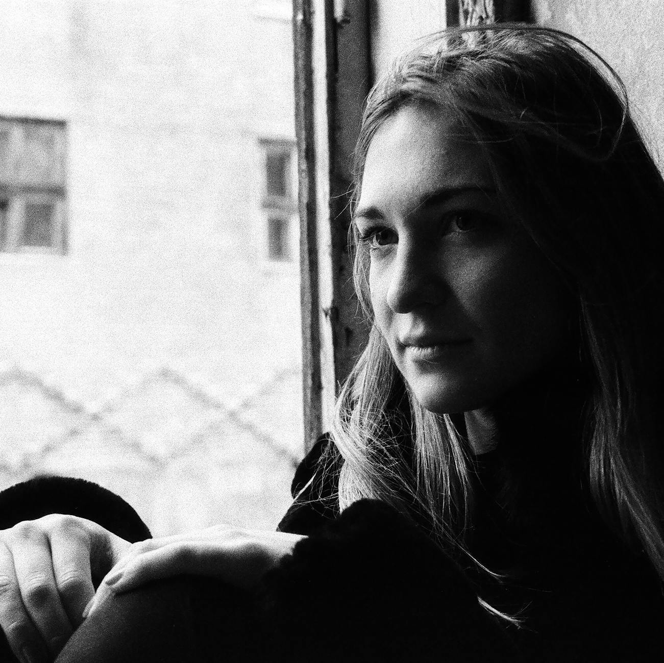 Black and white portrait of a woman gazing through a window in Lviv, Ukraine.