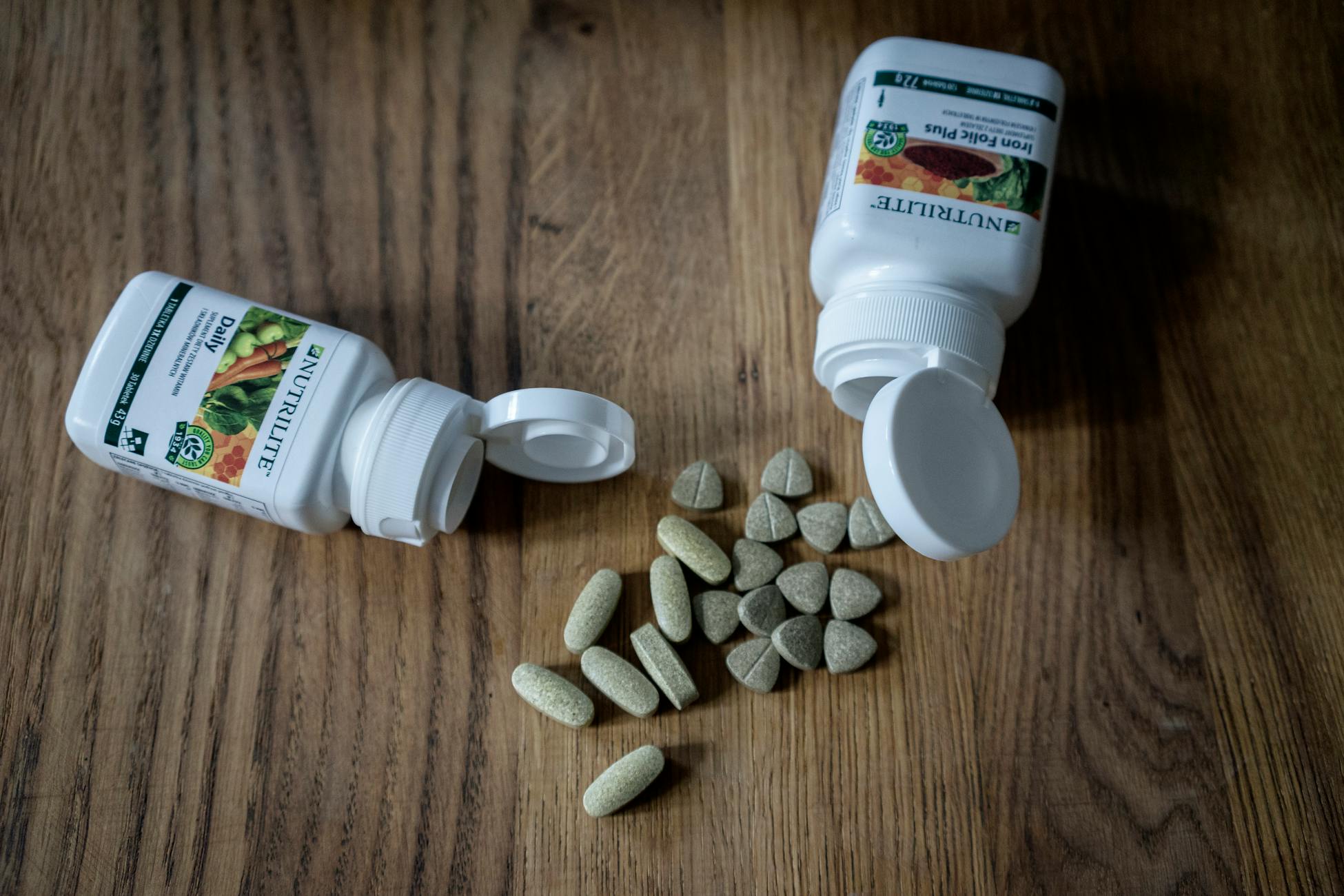 Variety of supplements and vitamin pills with open containers on a wooden surface.