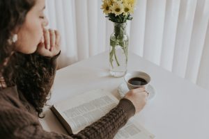Woman enjoying a peaceful moment with a book and coffee at a table adorned with flowers.