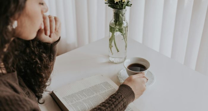 Woman enjoying a peaceful moment with a book and coffee at a table adorned with flowers.