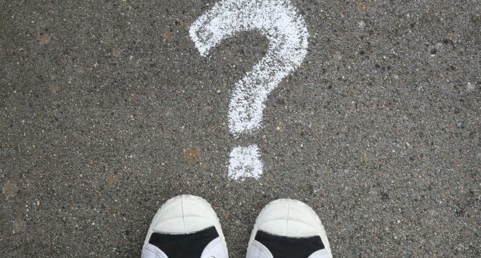 Sneakers on pavement with a chalk question mark, symbolizing curiosity or decisions.