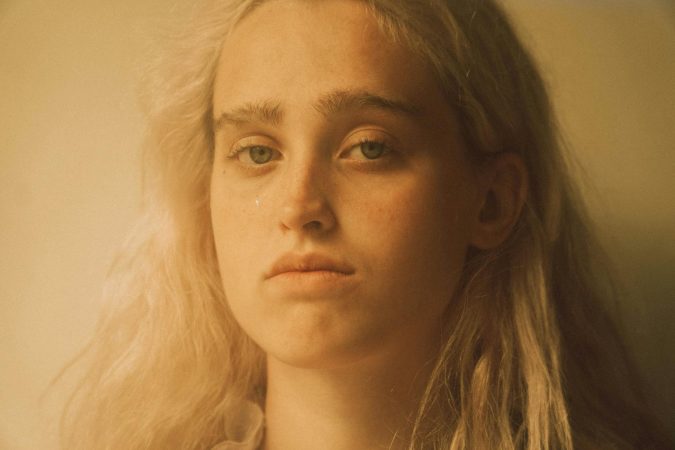 Close-up portrait of a young woman with a tear, conveying deep emotion in soft lighting.
