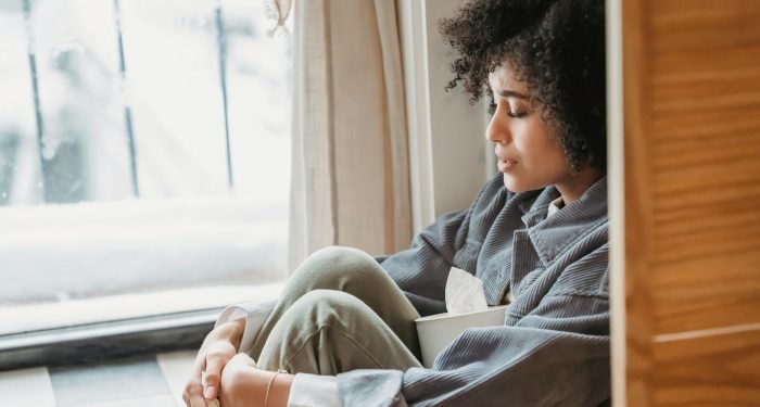 A young woman with curly hair sits alone by a window, lost in thought.