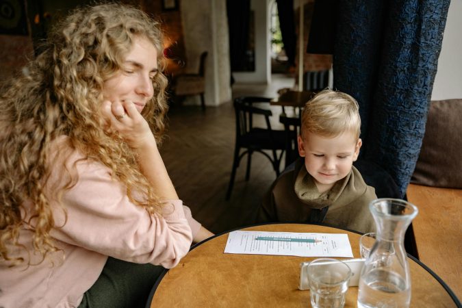 A woman and a young boy engage in a cozy moment at a cafe table, indoors.