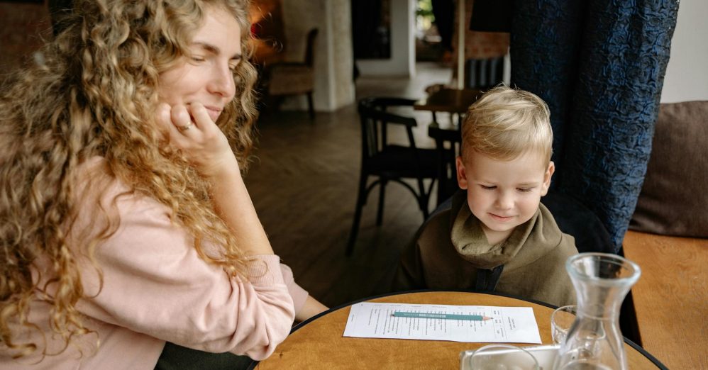 A woman and a young boy engage in a cozy moment at a cafe table, indoors.