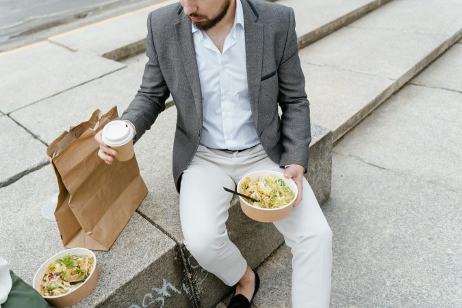 Man in a suit enjoying a takeaway salad and coffee outdoors on city steps.