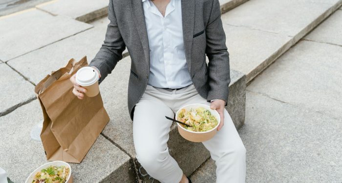 Man in a suit enjoying a takeaway salad and coffee outdoors on city steps.