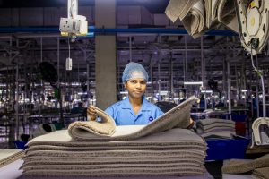 A female worker arranges fabrics in a busy textile factory interior.