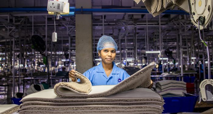 A female worker arranges fabrics in a busy textile factory interior.