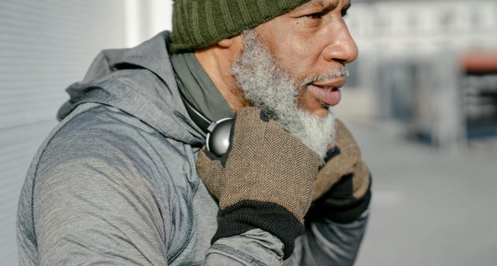 Side view of bearded elderly African American male in green knitted hat wit headphones on neck looking away