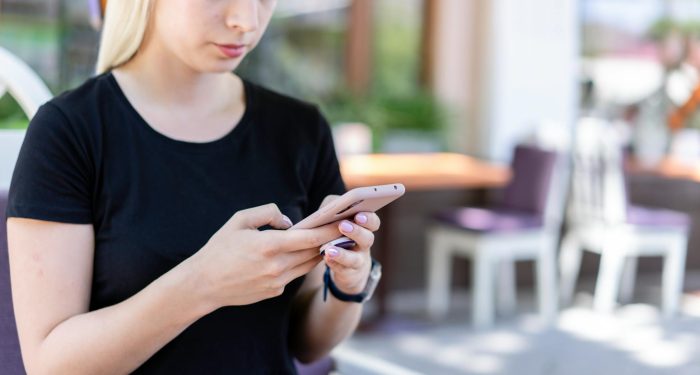 Young woman in a black shirt texting on her smartphone at an outdoor cafe.