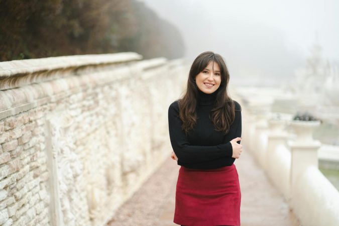 Portrait of a smiling woman in a red skirt and black sweater on a misty autumn day.