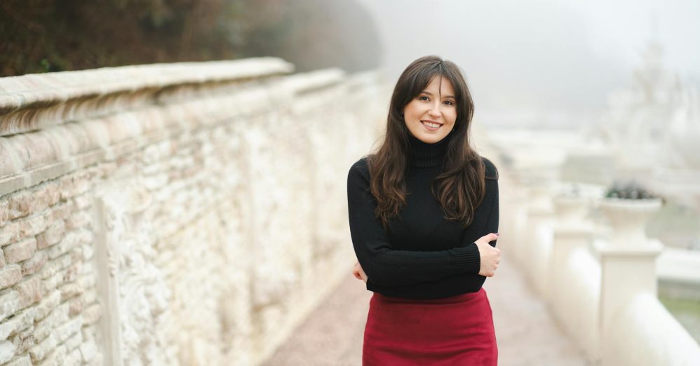Portrait of a smiling woman in a red skirt and black sweater on a misty autumn day.