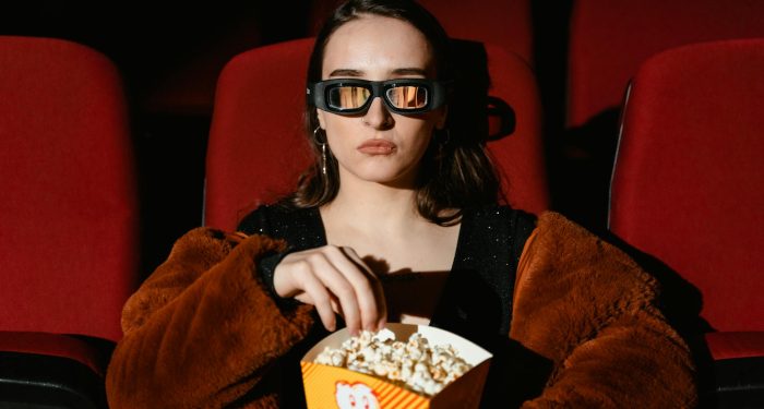 A woman in a fur coat enjoying popcorn while watching a 3D movie in a cinema.