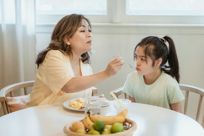 A mother lovingly feeds her daughter breakfast in a cozy home setting.