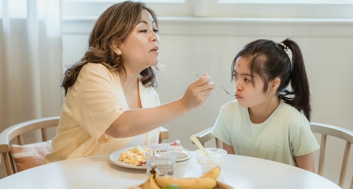 A mother lovingly feeds her daughter breakfast in a cozy home setting.