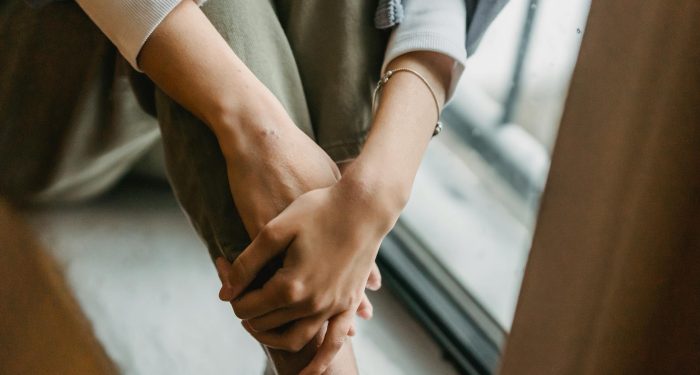 High angle of lonely crop anonymous female with bracelet standing with crossed legs and hands near window
