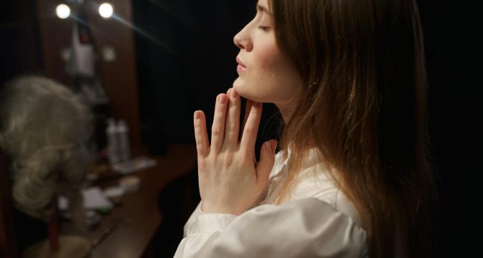 Side view of a woman with hands clasped in prayer, reflecting in a dressing room mirror.