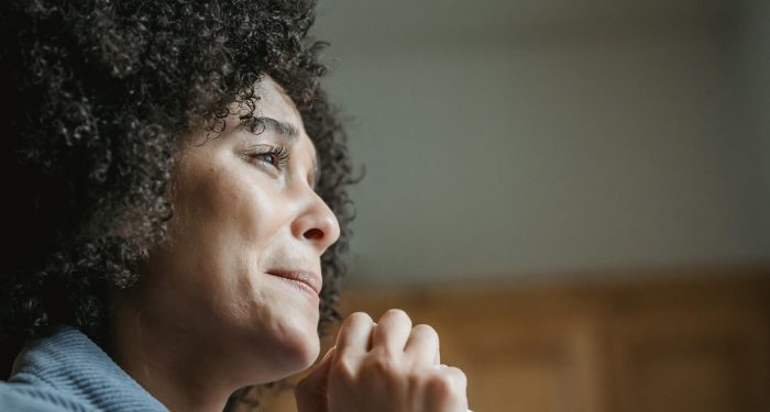 Low angle side view of crop depressed young African American female millennial with dark curly hair crying emotionally and looking away