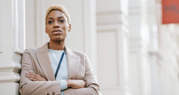 Young self assured African American female entrepreneur with folded arms looking forward near building column in city
