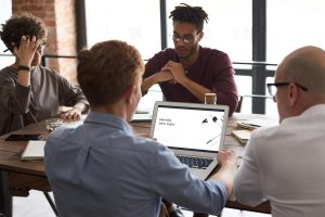 Team of diverse professionals brainstorming around a laptop in a modern office setting.