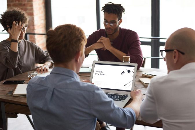 Team of diverse professionals brainstorming around a laptop in a modern office setting.