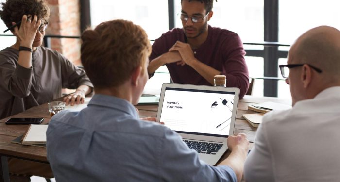 Team of diverse professionals brainstorming around a laptop in a modern office setting.
