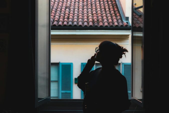 Silhouette of a woman in a serene moment by the window, viewing the tiled roof outside.