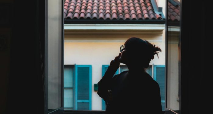 Silhouette of a woman in a serene moment by the window, viewing the tiled roof outside.