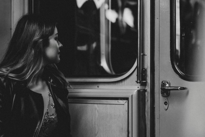 A woman in a black jacket gazes thoughtfully out a train window in monochrome.