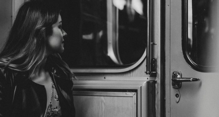 A woman in a black jacket gazes thoughtfully out a train window in monochrome.