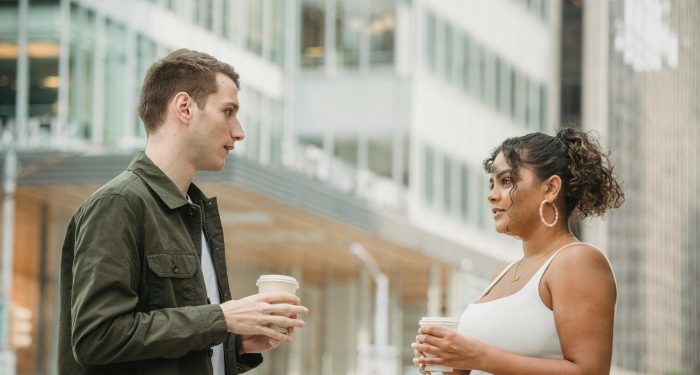 Two young adults enjoying a coffee break outdoors, engaging in conversation amidst an urban setting.