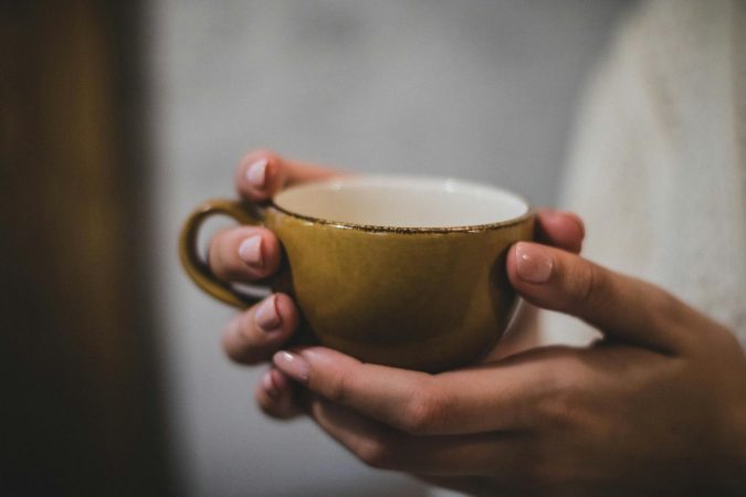 Warm brown coffee mug held in hands indoors, providing a cozy feel.