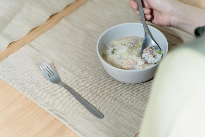 A hand holding a spoon with porridge in a bowl on a neatly set table.