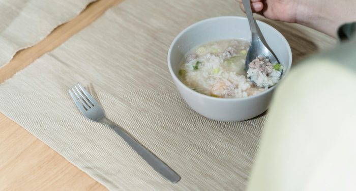 A hand holding a spoon with porridge in a bowl on a neatly set table.