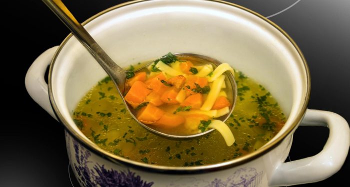Warm chicken noodle soup with vegetables served in a decorative ceramic pot, perfect for a cozy winter meal.