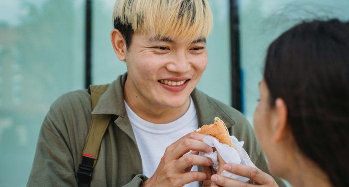 Smiling couple sharing a delicious street food snack outdoors.