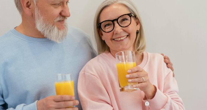 Smiling elderly couple holding glasses of fresh orange juice indoors.