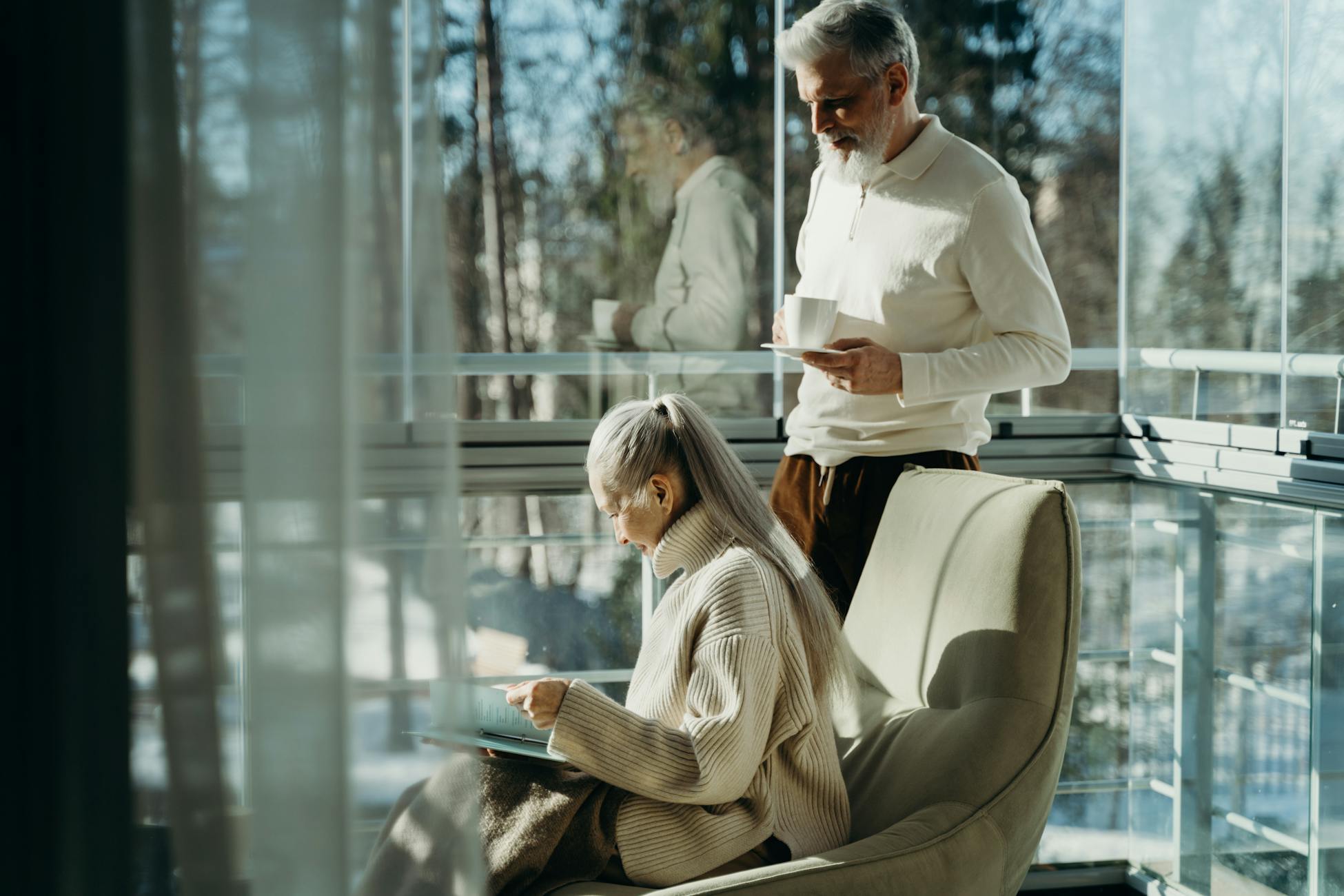 Elderly couple enjoying a serene moment indoors with natural lighting, sipping coffee.