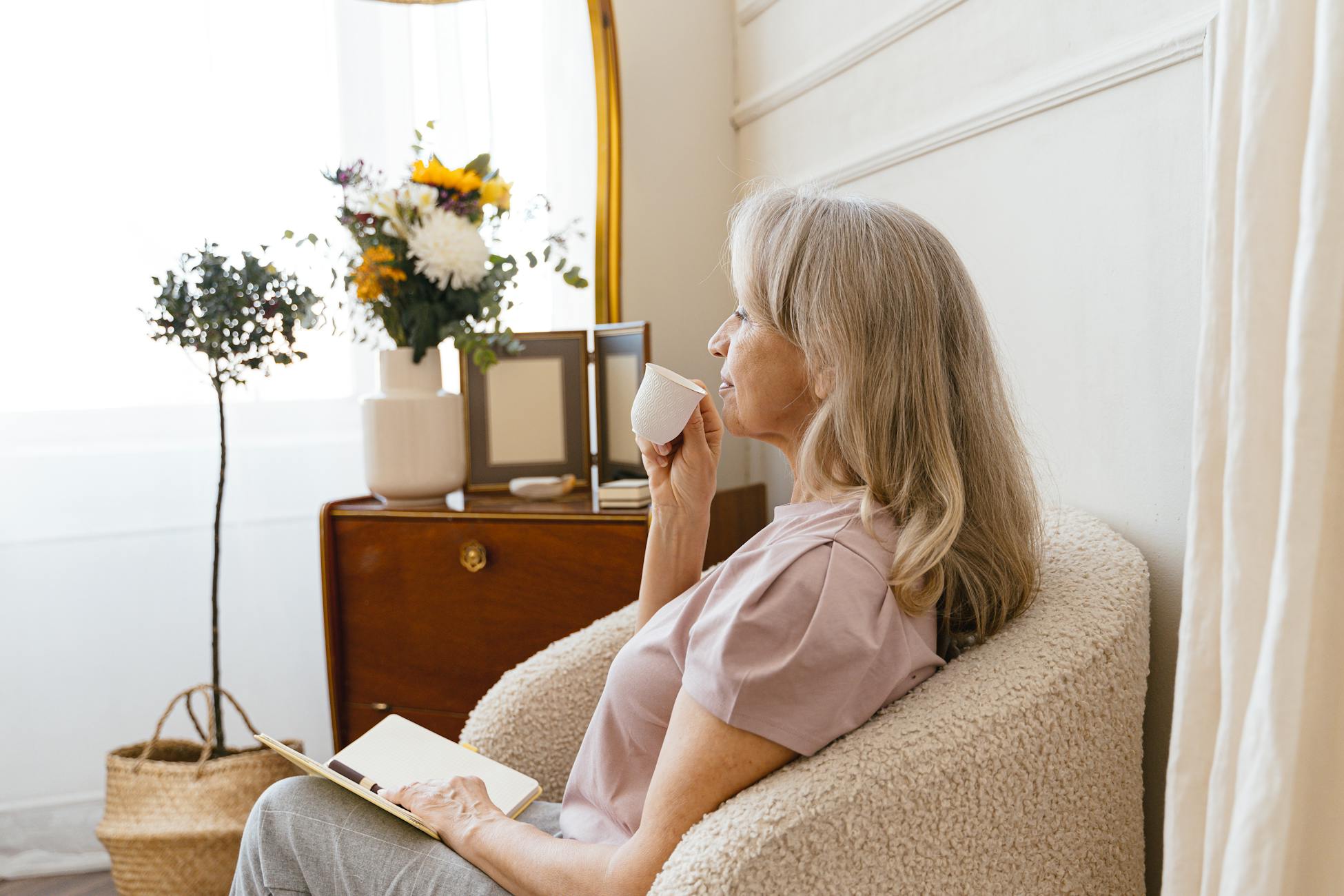 Senior woman relaxes with a cup of tea in a cozy indoor setting, side view.