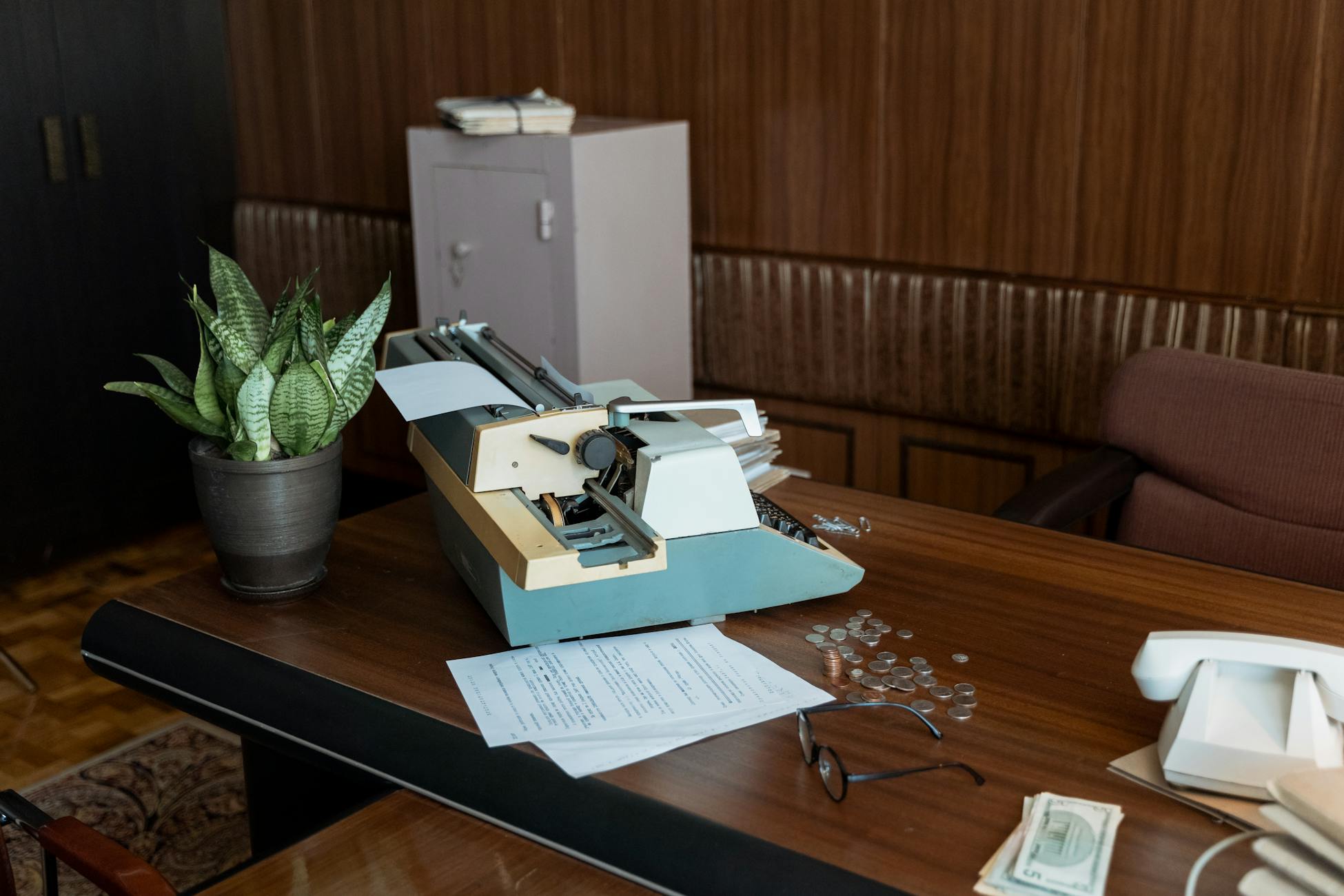 Retro office setting with a vintage typewriter, papers, and coins on a wooden desk.
