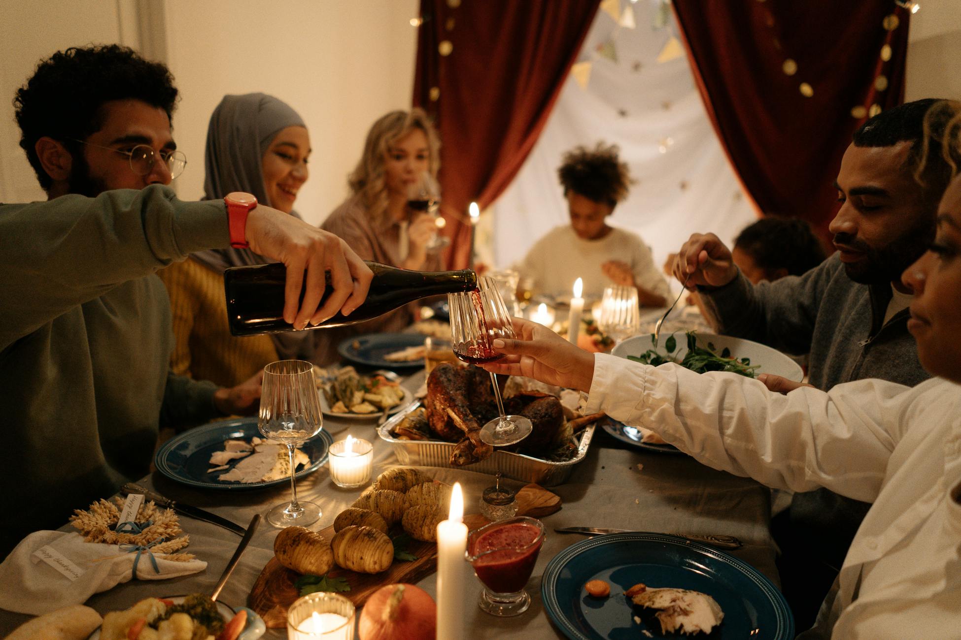 A family enjoying a festive dinner together, pouring wine with candles lit indoors.