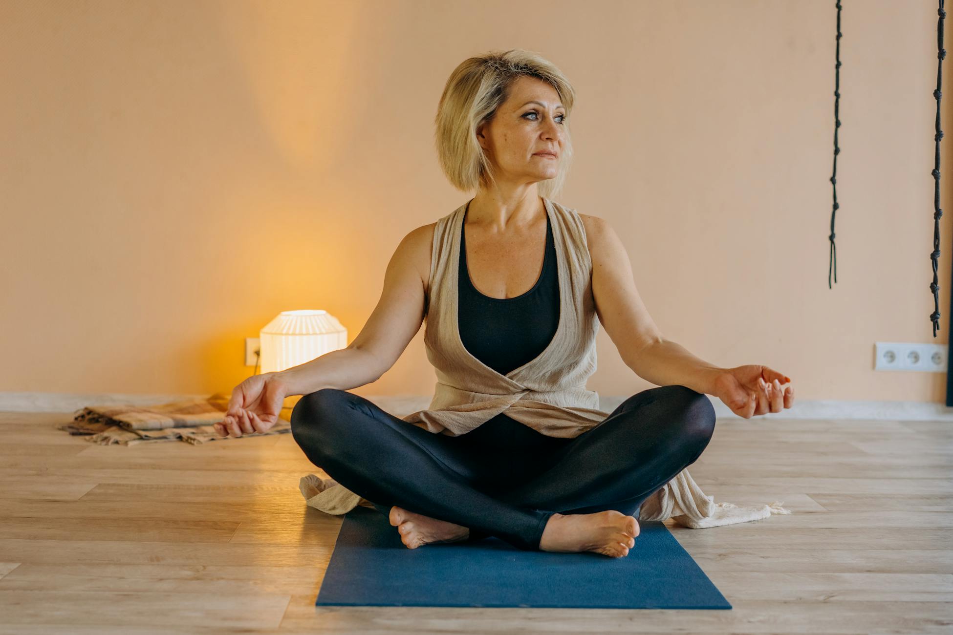 A senior woman sits in a yoga pose indoors, promoting mindfulness and healthy living.