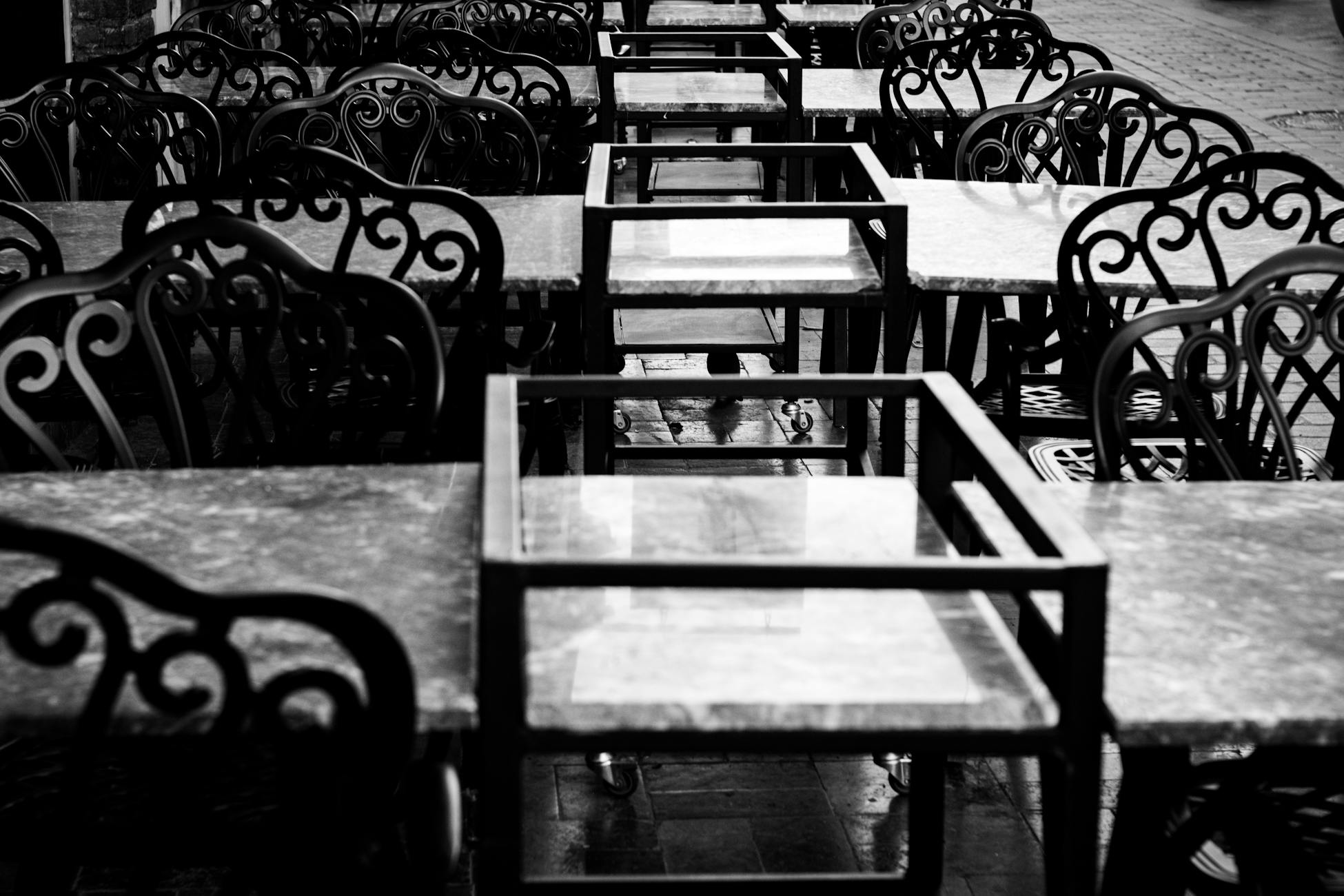 Empty outdoor cafe tables and ornate chairs in black and white.