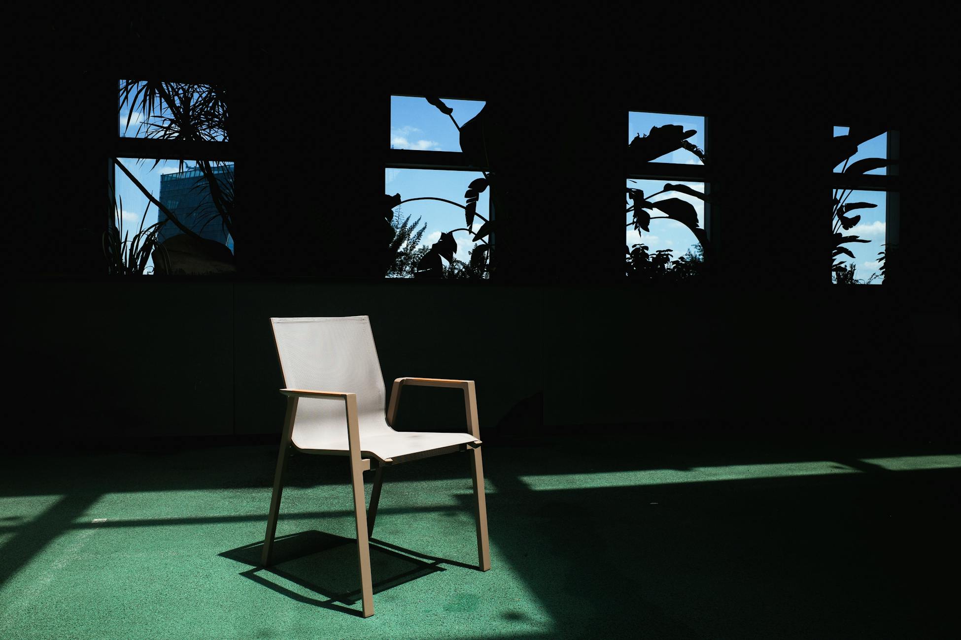 Minimalist chair in shadowy room with lush outdoor view through windows.